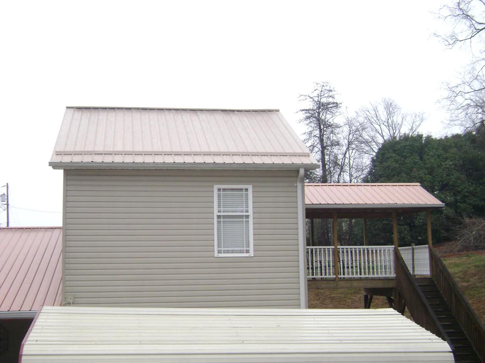 Tan metal roofs on a two story addition and attached porch, from a Roof Replacement job in Sheffield